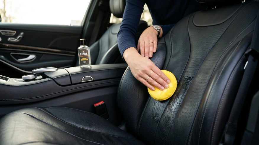 Person applying leather conditioner to a car seat with a microfiber cloth.