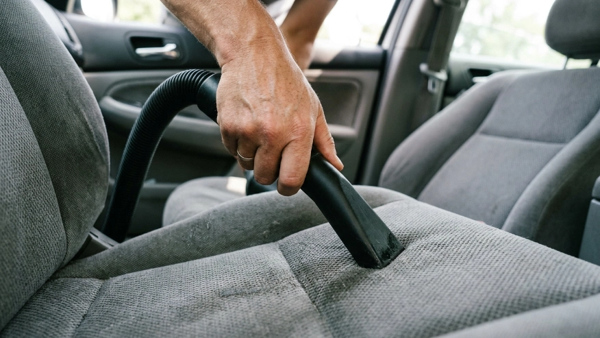 A person using a wet-dry shop vacuum nozzle on a car seat to extract moisture and cat urine odor