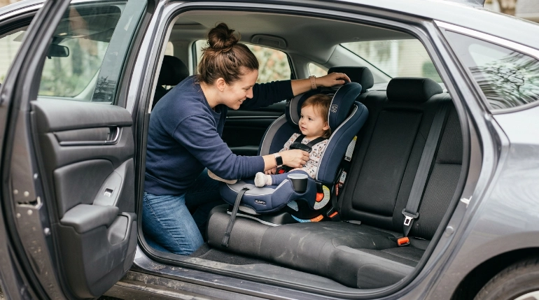 Parent adjusts the headrest and harness on a narrow Evenflo-style four-stage convertible car seat