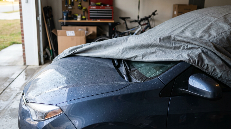 Condensation droplets beneath a breathable car cover on a cool vehicle inside a residential garage.